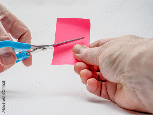 Man cutting pink craft paper with blue left handed scissors selected focus photo