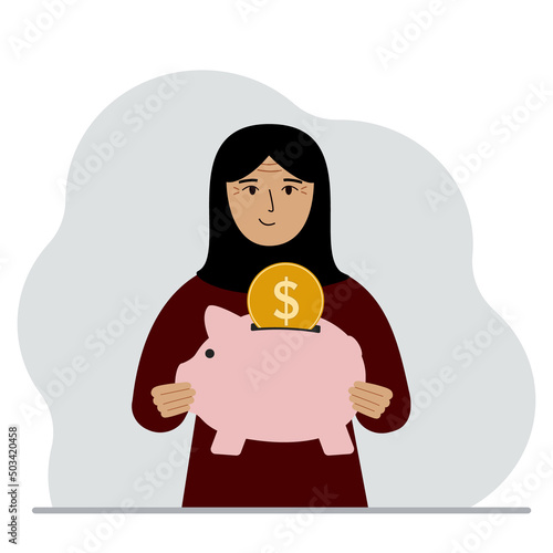 Happy muslim woman holds a piggy bank, a coin falls into the piggy bank. The concept of saving finance, savings, investing finances.