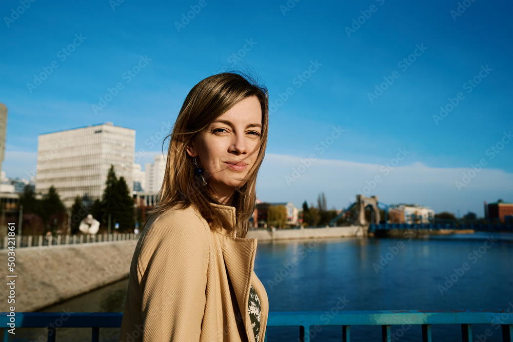 Millennial caucasian woman standing at riverfront and enjoy with sunny day, Female tourist wearing stylish trench walking at european city street