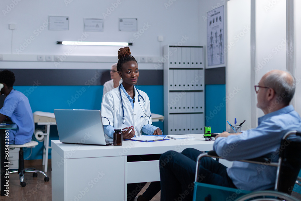Obraz premium Healthcare clinic medic expert conversating with sick senior patient in wheelchair about illness symptoms and treatment schedule. Hospital doctor talking with elder person with disability about