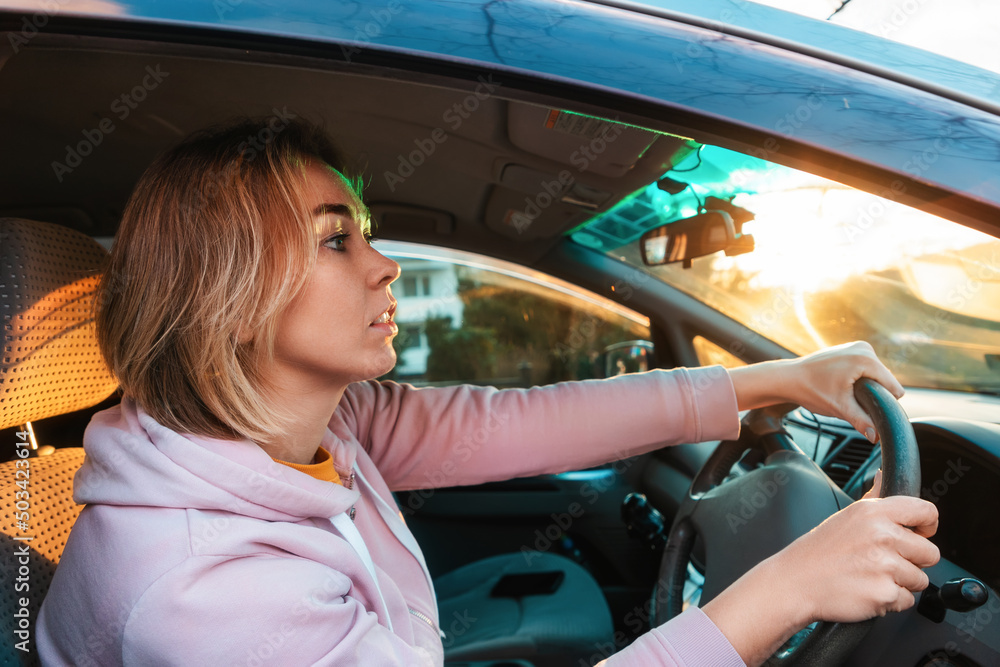 Portrait of young caucasian woman is sitting at the wheel of a right-handed car and anxiously looks at the road. Traffic rules concept