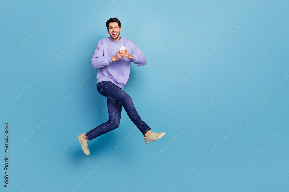 Photo of cheerful guy jump use gadget rush eshop application adverts isolated blue pastel color background Photo of cheerful guy jump use gadget rush eshop application adverts isolated blue pastel color background