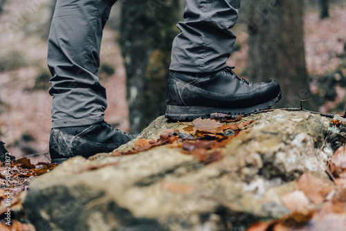 Close up detail photo of hiking or trekking boots in muddy autumn trail. Mountain leather shoes on dirty terrain, wet ground and stepping into water. Waterproof shoes using goretex technology. photo