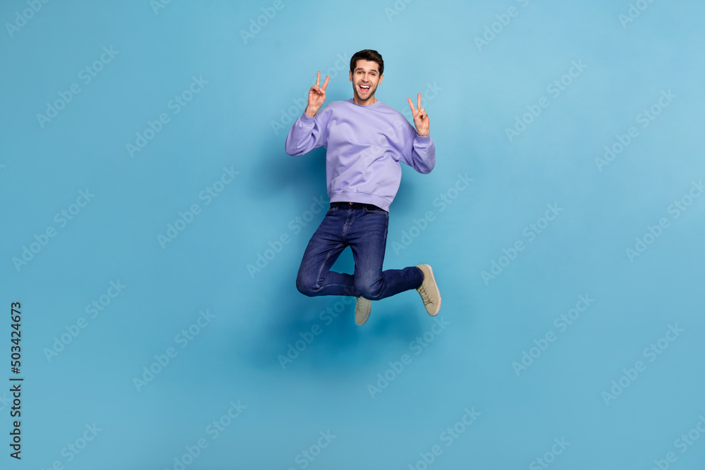 Full length body size view of attractive cheery guy hippie jumping showing double v sign isolated over bright blue color background