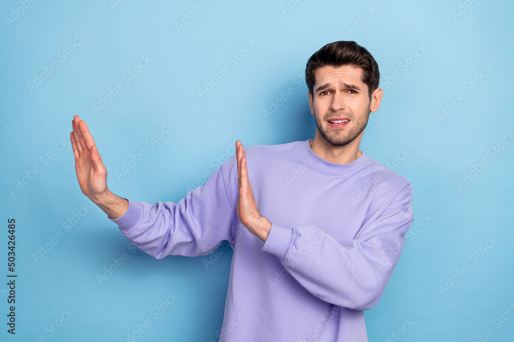 Photo of sad young brunet guy show stop wear sweater isolated on blue color background Photo of sad young brunet guy show stop wear sweater isolated on blue color background