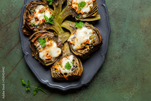 Baked Stuffed Artichoke with vegetables, onion, carrot, parsley, bechamel sauce and parmesan cheese. Dark green table surface. Top view. photo