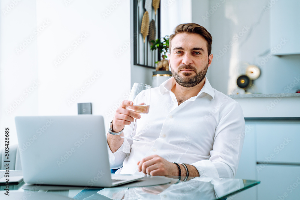 Portrait of handsome businessman using laptop in modern kitchen, drinking beverage, work very easy, writing message.