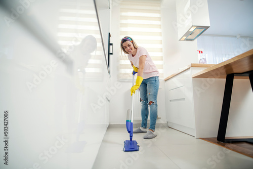 A happy housewife cleaning kitchen floor at home.