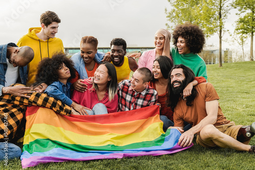 Happy diverse friends holding LGBT rainbow flag having fun together outdoors - Focus on right man with leg prosthesis