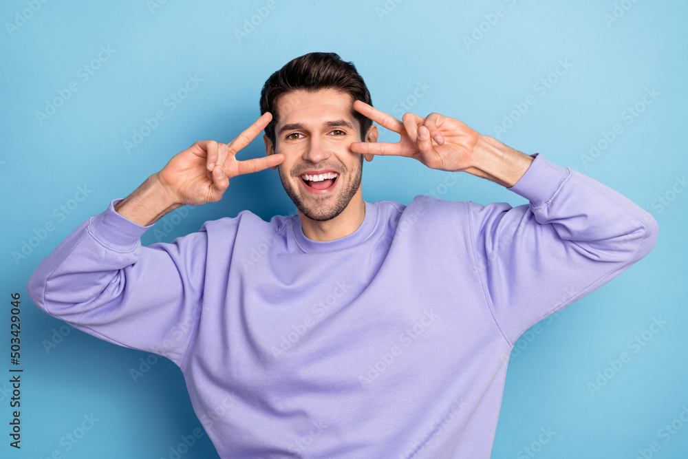 Photo of cool millennial brunet guy show v-sign wear sweatshirt isolated on blue color background Photo of cool millennial brunet guy show v-sign wear sweatshirt isolated on blue color background