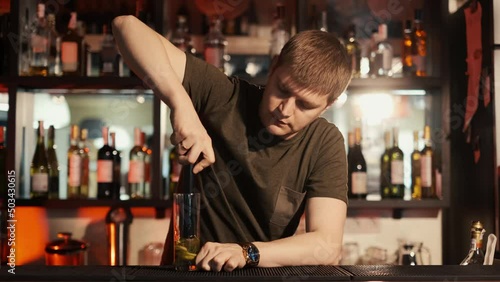 A professional bartender is preparing an alcoholic cocktail with ice cubes to customers at the bar or disco club.