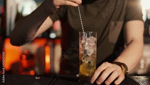 A professional bartender is preparing an alcoholic cocktail with ice cubes to customers at the bar or disco club.