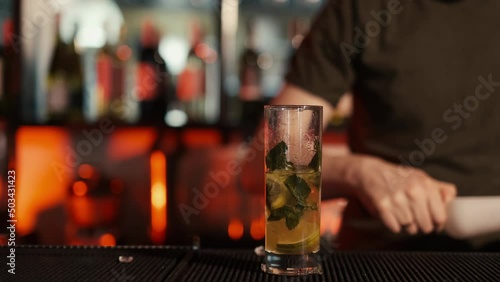 A professional bartender is preparing an alcoholic cocktail with ice cubes to customers at the bar or disco club.