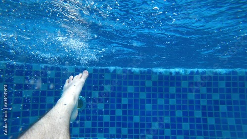 The guy pushes off from the side of the pool with his feet and swims. The video begins with a waterfall in a blue pool. Splashes of water fall on the lens. Bubbles form from the movement of the legs photo