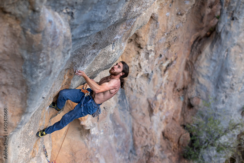 a strong man climbs a difficult climbing route