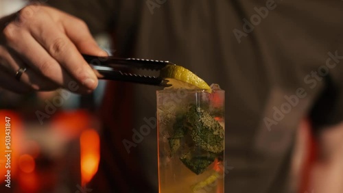 A professional bartender is preparing an alcoholic cocktail with ice cubes to customers at the bar or disco club.