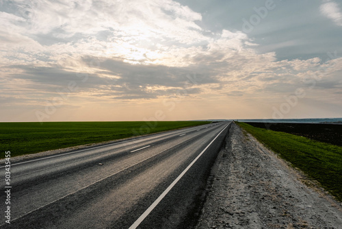 Outdoor Empty Asphalt Road and Green Field Meadow at Sunset. Sun and Clouds on Background. © Артём Ковязин