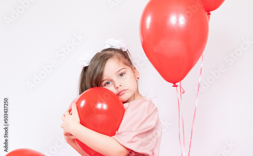 Cute little girl holding a bunch of red heart-shaped balloons
