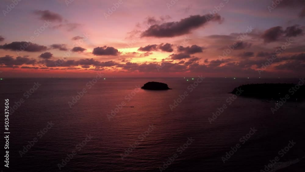 Golden-orange sunset with a view of the sea and the island. Small waves. The rays of the sun and clouds are reflected in the water. A lonely island stands in the distance. A boat is sailing. Phuket Golden-orange sunset with a view of the sea and the island. Small waves. The rays of the sun and clouds are reflected in the water. A lonely island stands in the distance. A boat is sailing. Phuket