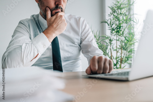 Businessman during video call, looking at laptop screen and listening to a speaker photo