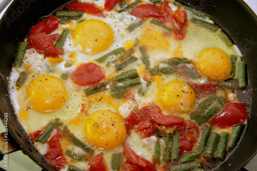 Morning roasted whole eggs on the black pan and with tomato and green beans