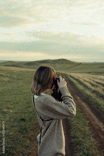 beautiful woman walking on field at sunset with retro photo camera  