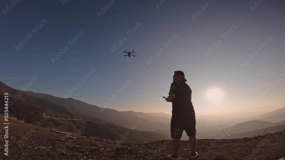 Young man takes off drone from his hand to work with videos and photos. Modern entertainment for future generation. Silhouette of man in sunset. Enjoy the technology in the midst of natural landscapes Young man takes off drone from his hand to work with videos and photos. Modern entertainment for future generation. Silhouette of man in sunset. Enjoy the technology in the midst of natural landscapes