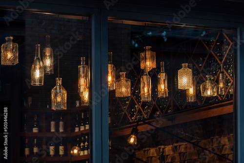 Lanterns made of glass bottles and Edison lamp bulbs. DIY lamps made from recycled old bottles hanging in cafe window.