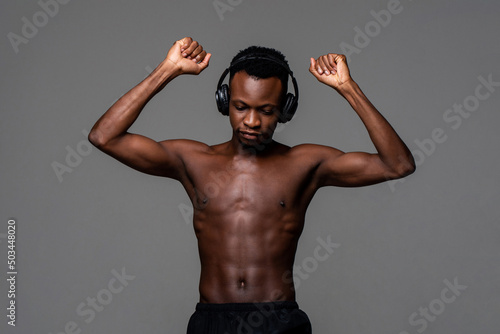Shirtless African man with headphone listening to music while standing on gray isolated background in studio