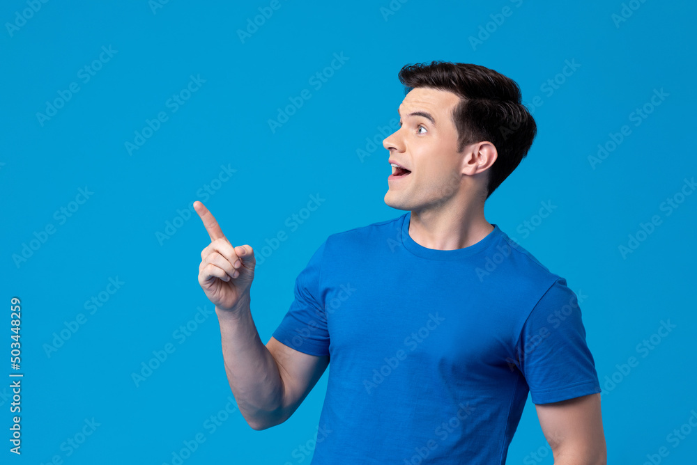 Excited young Caucasian man looking sideways and pointing up in light blue isolated background Excited young Caucasian man looking sideways and pointing up in light blue isolated background