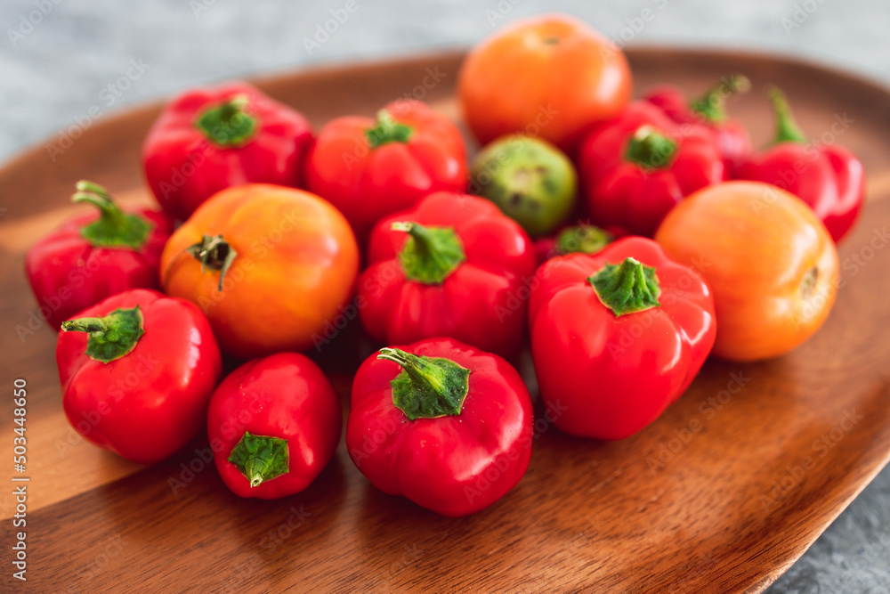 freshly picked mini capsicums and tomatoes with vibrant red and orange tones on wooden tray, simple ingredients concept freshly picked mini capsicums and tomatoes with vibrant red and orange tones on wooden tray, simple ingredients concept