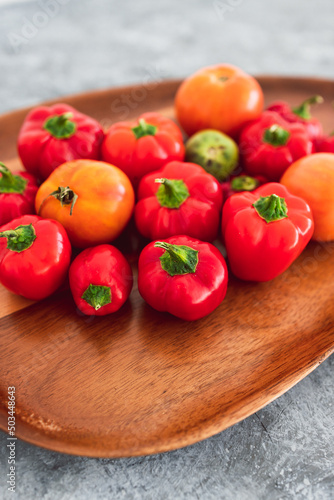 freshly picked mini capsicums and tomatoes with vibrant red and orange tones on wooden tray, simple ingredients concept