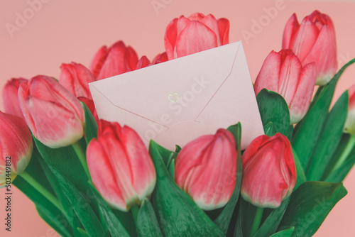 Fototapeta Naklejka Na Ścianę i Meble -  pink paper envelope with a heart in a bright spring bouquet of pink tulips, the concept of romance, gift and holiday greetings