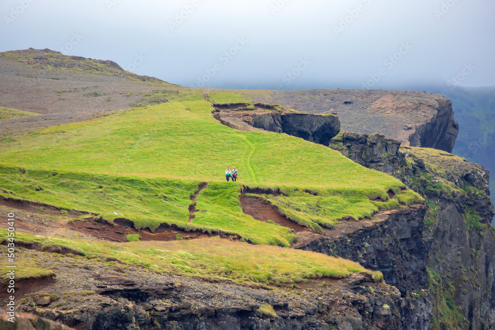 Two people are walking along the mountain green slope of Iceland. Travel and tourism
