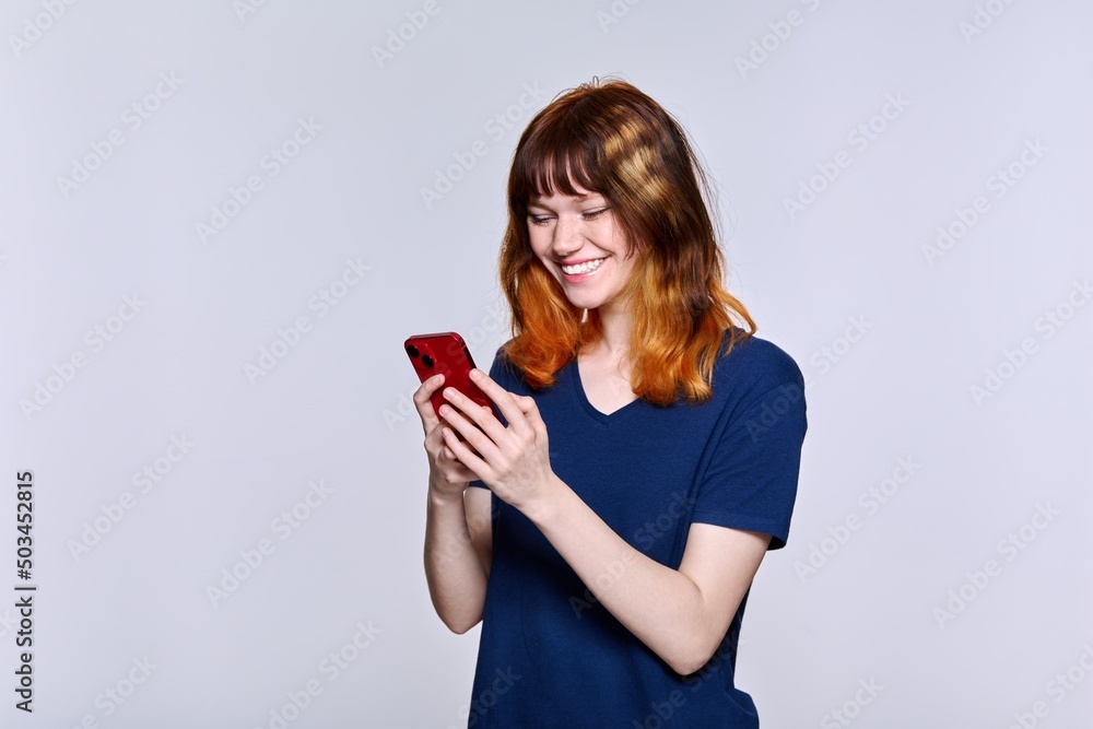 Smiling teenage female looking at smartphone screen, on light studio background Smiling teenage female looking at smartphone screen, on light studio background