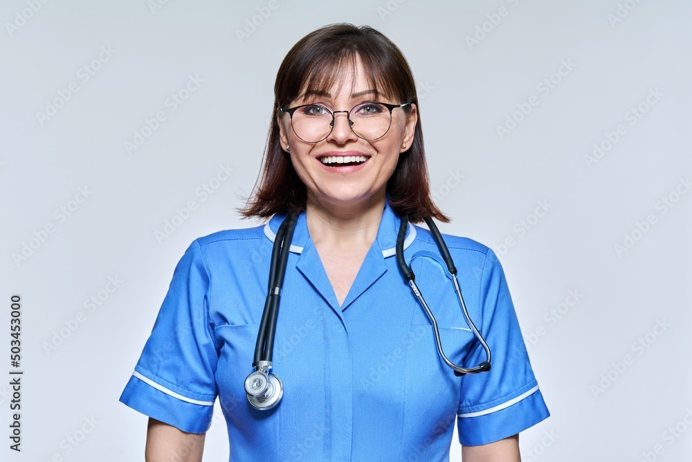 Headshot portrait of nurse in blue uniform looking at camera on light studio background Headshot portrait of nurse in blue uniform looking at camera on light studio background