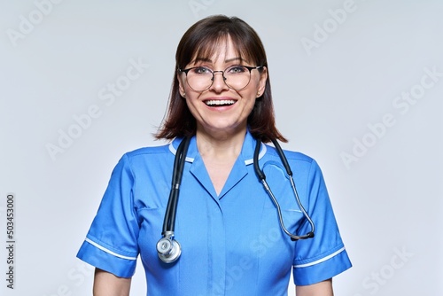 Headshot portrait of nurse in blue uniform looking at camera on light studio background photo