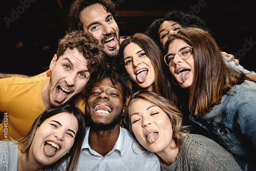 Portrait of happy friends embracing and making grimaces tongue out looking at the camera - people having fun, diversity, inclusion and integration lifestyle concept
