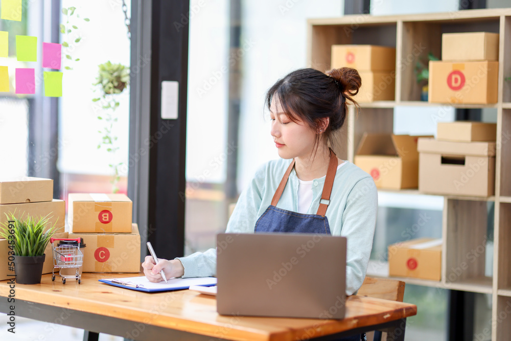 Startup small business entrepreneur or freelance Asian woman using a laptop with box, Young success Asian woman with her hand lift up, online marketing packaging box and delivery, SME concept. Startup small business entrepreneur or freelance Asian woman using a laptop with box, Young success Asian woman with her hand lift up, online marketing packaging box and delivery, SME concept.
