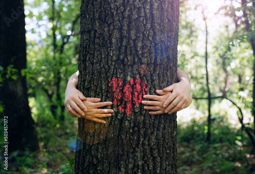 Family embracing the tree with red heart. Nature lover family.Concept of nature protection, care for environment. Environment day and earth day.