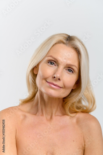 Vertical view of the attractive middle-aged blonde woman looking at the camera over white background  charming mature lady has beautiful smile
