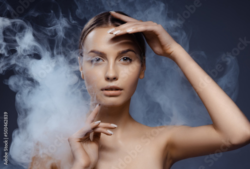 Portrait of beautiful young girl with clean, well kept skin isolated on dark background with smoke. Concept of beauty, art, ad, cosmetics