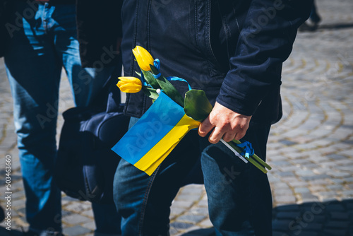 In the man's hand is a Ukrainian flag and flowers to honor the dead peaceful Ukrainians. 