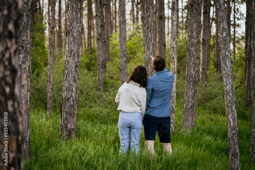 Young couple standing together in forest, with man pointing up. Man and woman looking at something interesting in the forest. © Marijan
