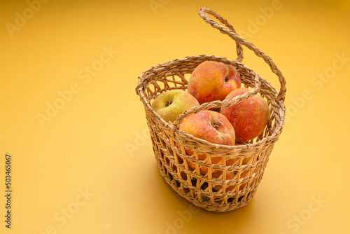 Group of fresh peaches fruits in a basket over a yellow background