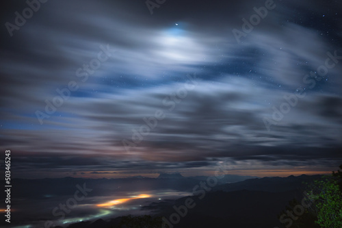 Landscape of cloudy blowing through blue sky with stars and moonlight over mountain peak in national park at night