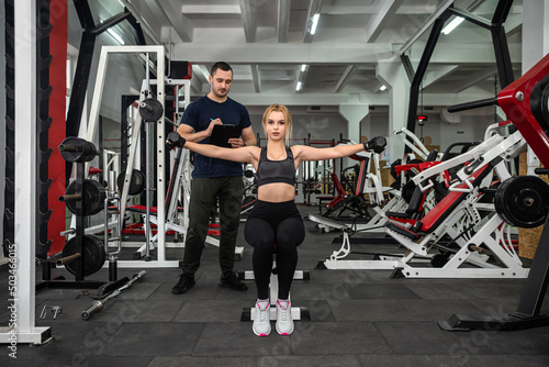 Fototapeta Naklejka Na Ścianę i Meble -  male trainer help her woman client working with dumbbell weights at  gym