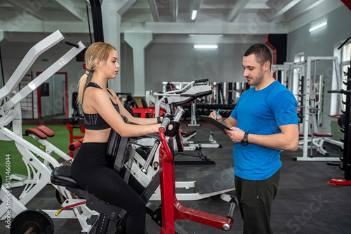The trainer assists with female client doing workout in the gym