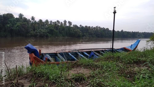 Wallpaper Mural Small old blue fishing boat tied to a light pole near riverside with green coconut trees background during kerala heavy wind and rain flood because of fast moving or flowing dirty brown river water. Torontodigital.ca