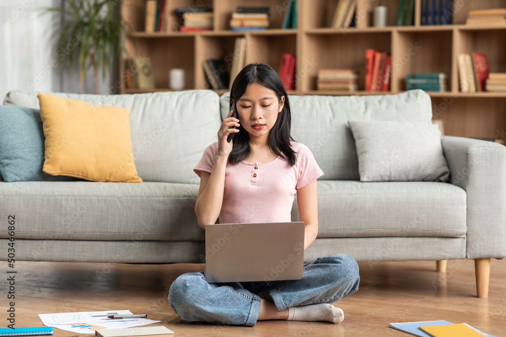 Asian female freelancer talking on cellphone and typing on laptop, working online from home, sitting on floor Asian female freelancer talking on cellphone and typing on laptop, working online from home, sitting on floor
